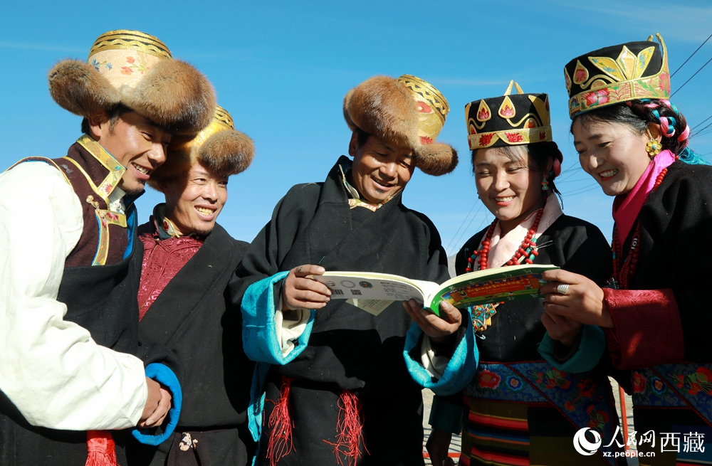 乡亲们身着民族盛装，围站在一起认真翻看日历，共话农事安排与时节规律，笑容洋溢传递丰收期盼。人民网记者 吴雨仁摄